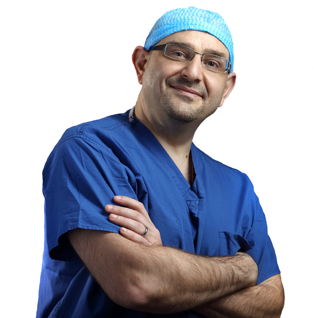 Chief of colorectal surgery Bashar Safar, wearing blue scrubs and a surgical cap, stands with his arms crossed, smiling. 